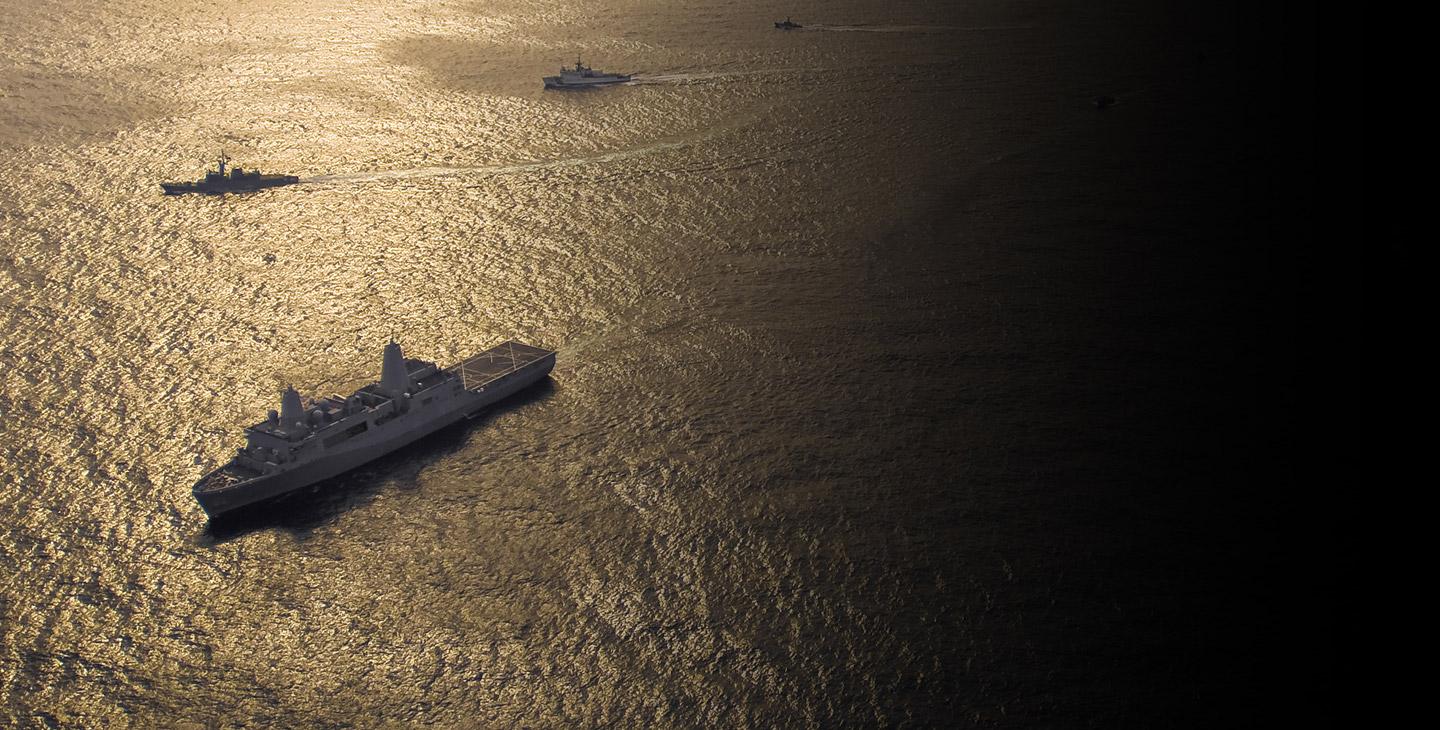 Military fleet of 4 traveling in the ocean at dusk utilizing maritime satellite services
