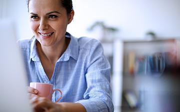Woman sitting in front of her computer, drinking coffee and smiling
