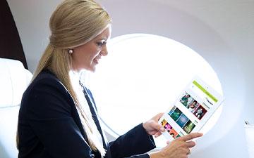 Blonde business woman sitting on a private jet looking at content on a tablet